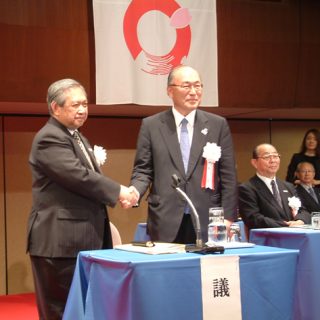 中村前会長（左）と握手する、新会長に就いた西田氏