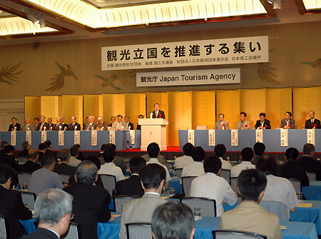 観光庁の英文名を背にあいさつする冬柴国交省。 国会議員、16団体のトップが壇上に並んだ