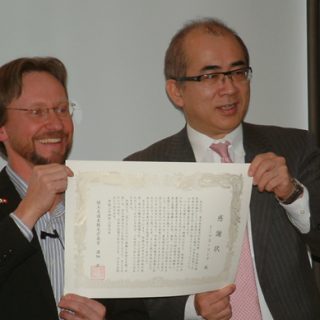 溝畑長官（右）とともに感謝状を披露するトーマスさん