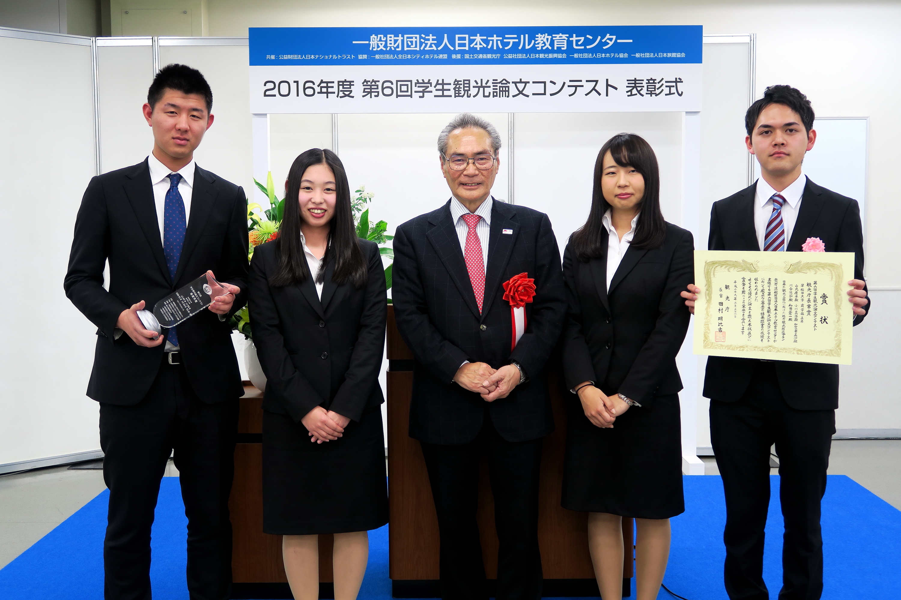 石塚理事長（中央）と最優秀賞の早大生